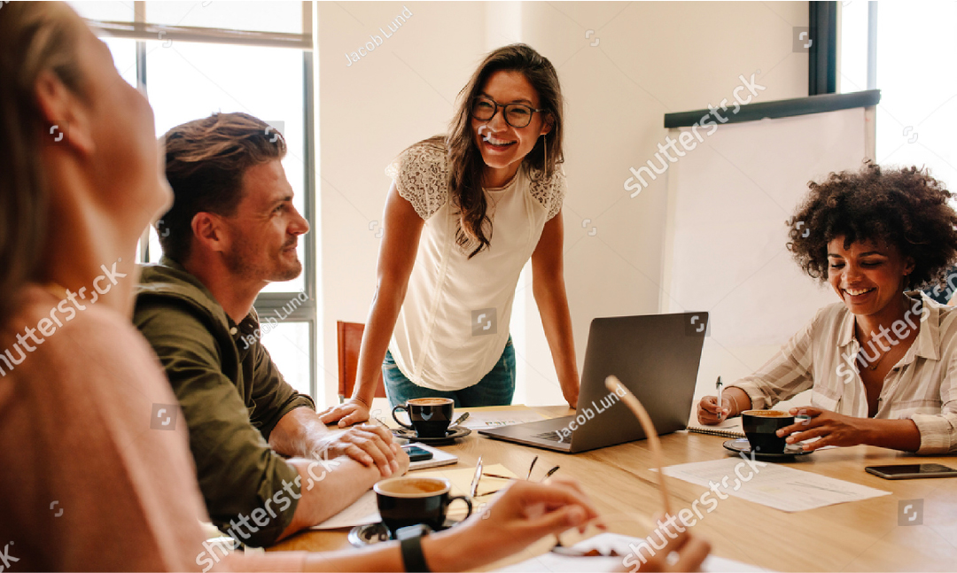 four professionals sitting around a table having a meeting while smiling