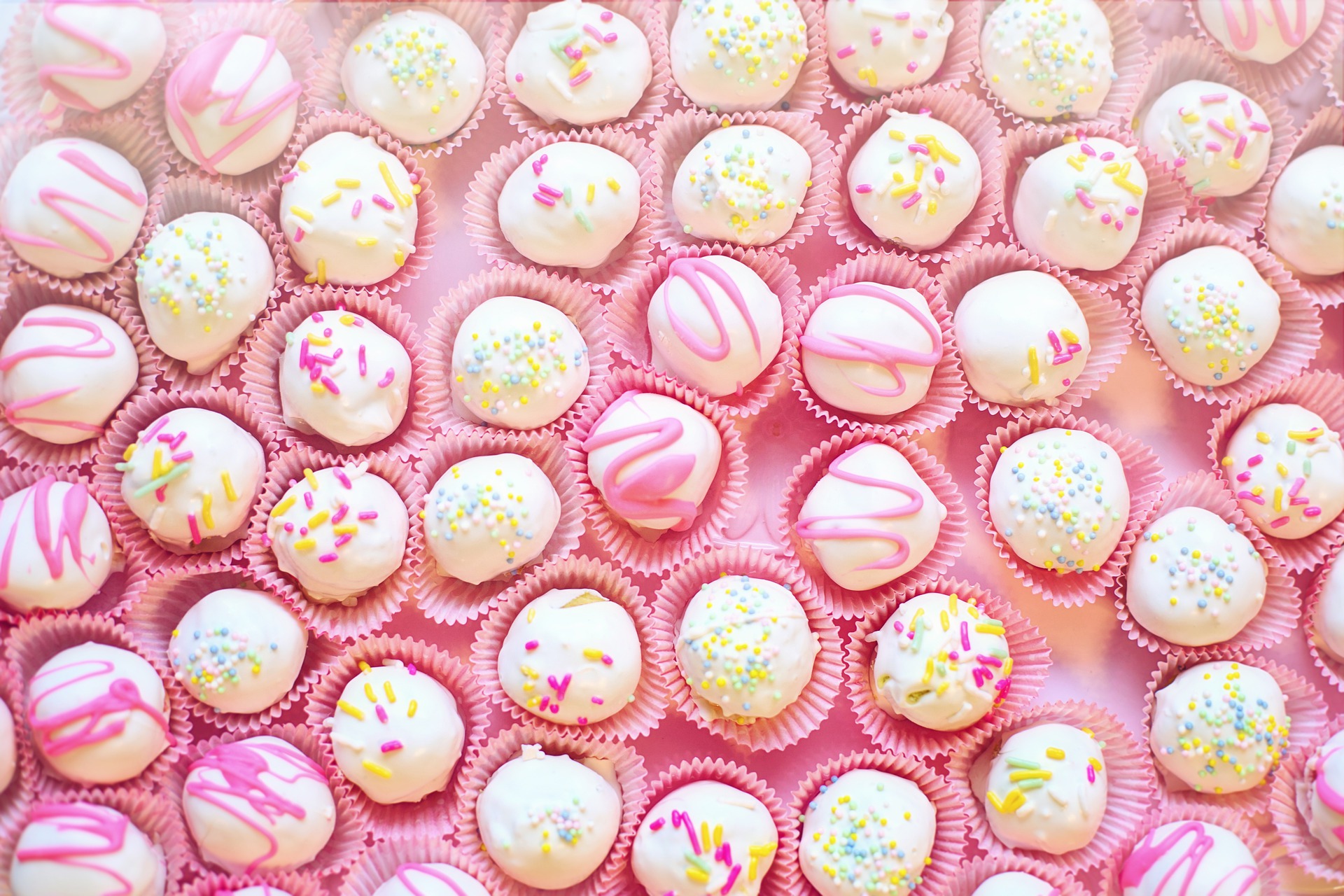 a large number of cakes shaped in a circular ball shape, with pink and white icing covering the top of them.