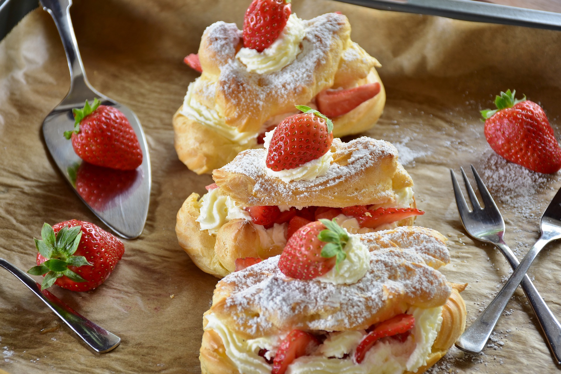 Two cream eclairs placed next to one another with cream and strawberries on the top of both.