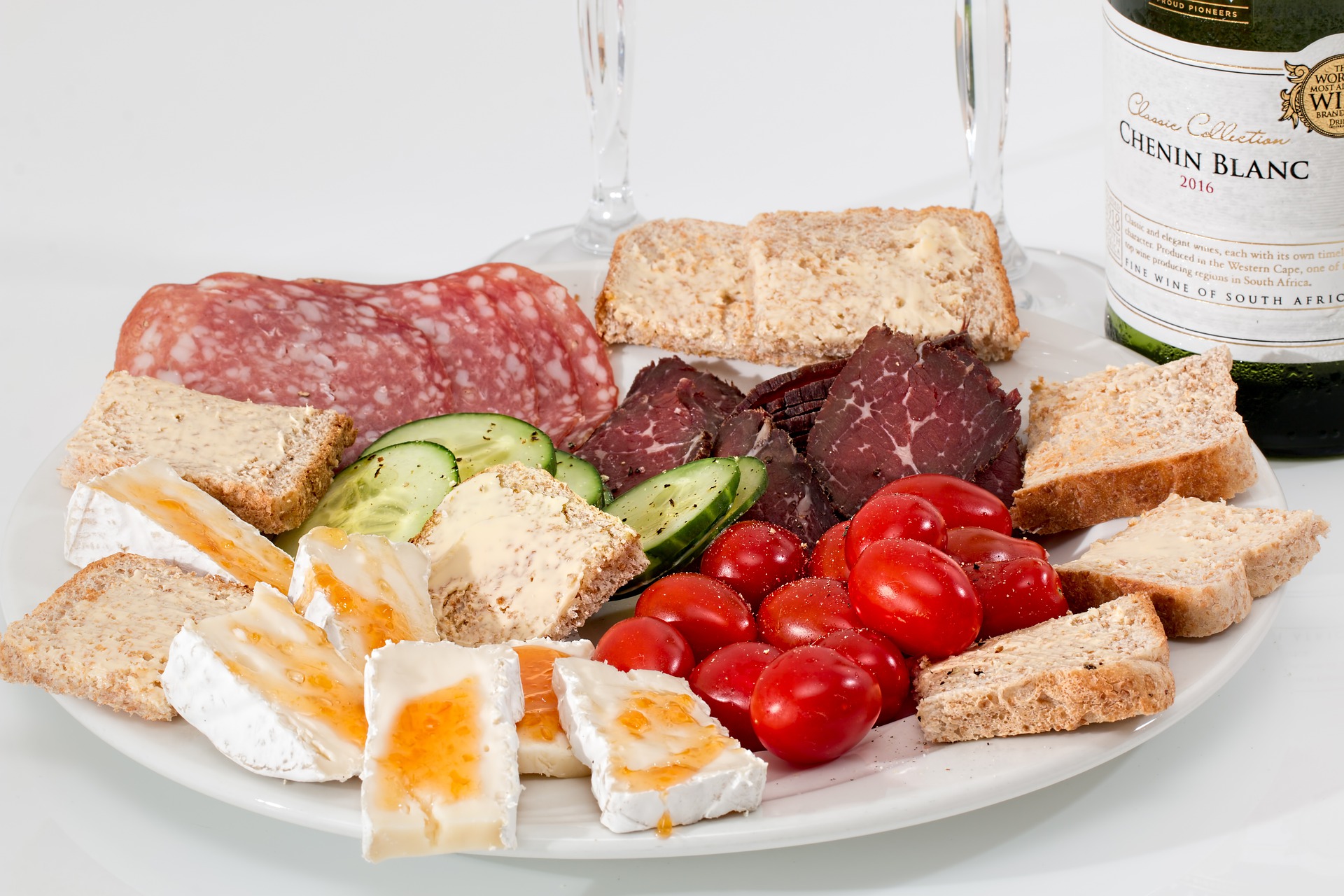 a selection of hors-doeuvre, including cheese, grapes and hams on a platter, with a black background.