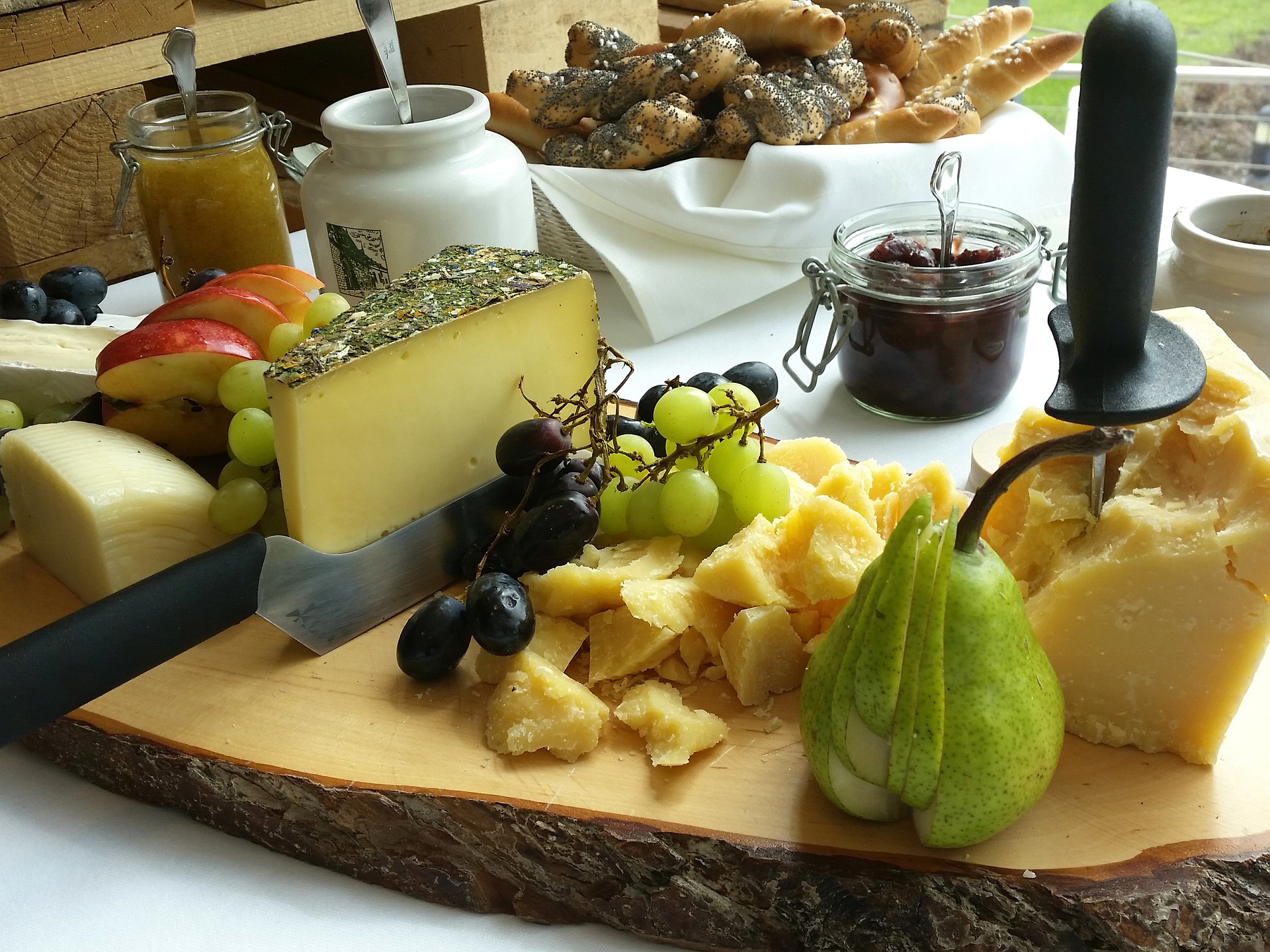 A buffet display of bread rolls, cheese, and chutney accompanied by fresh grapes, apples, and pears.