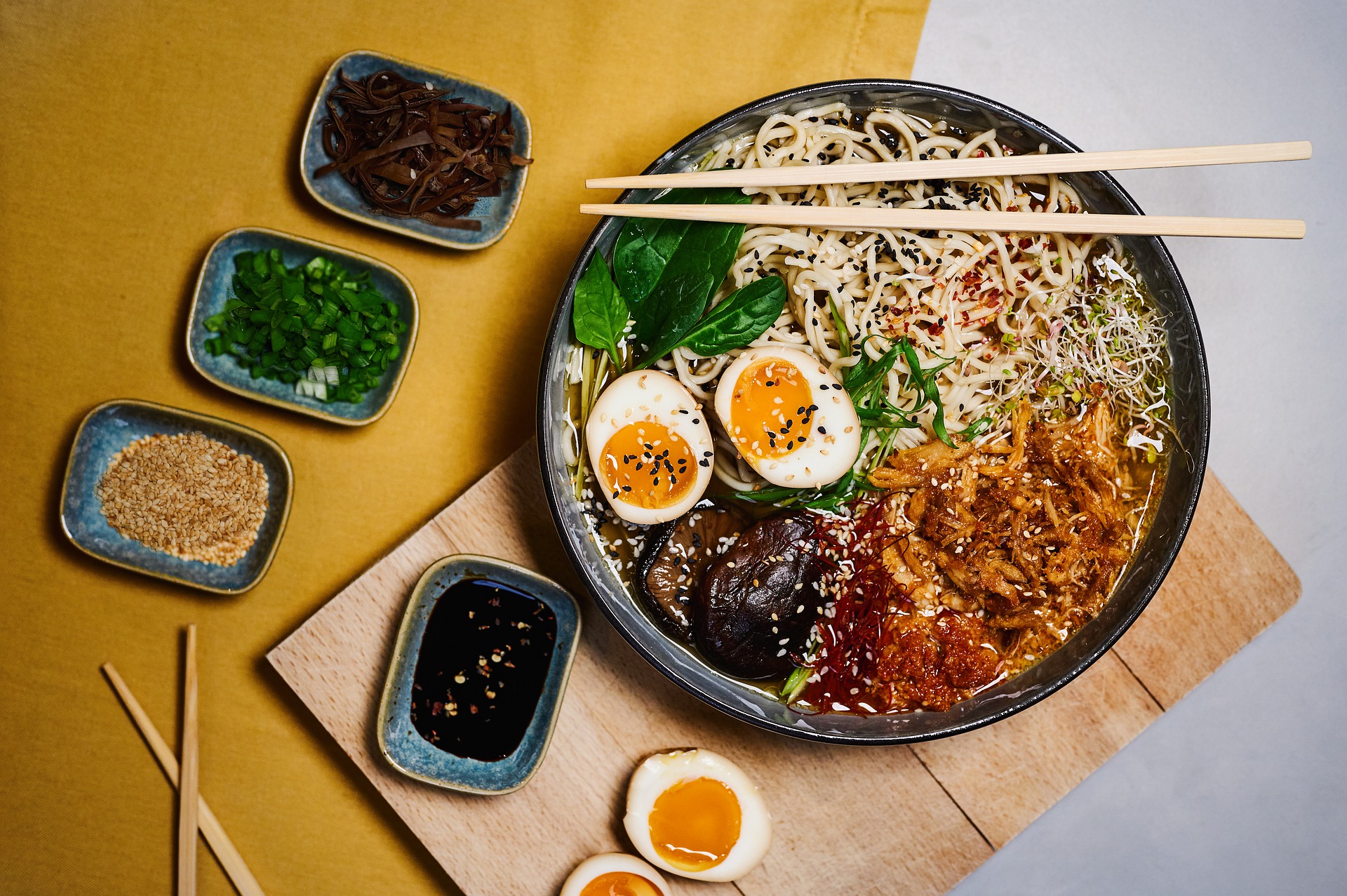 A bird's eye view of a ramen bowl filled with egg noodles, boiled egg, fresh spinach, sauteed mushrooms and marinated sliced chicken.