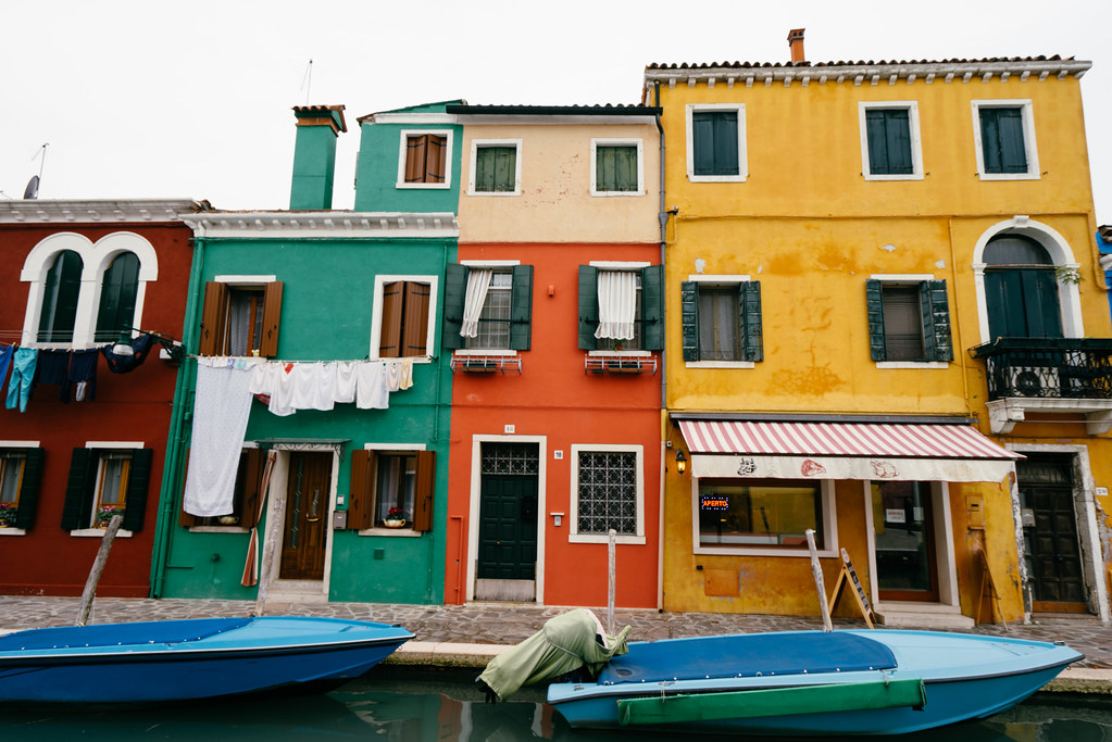 Four houses of different shapes and colors line a dock where a boat is anchored